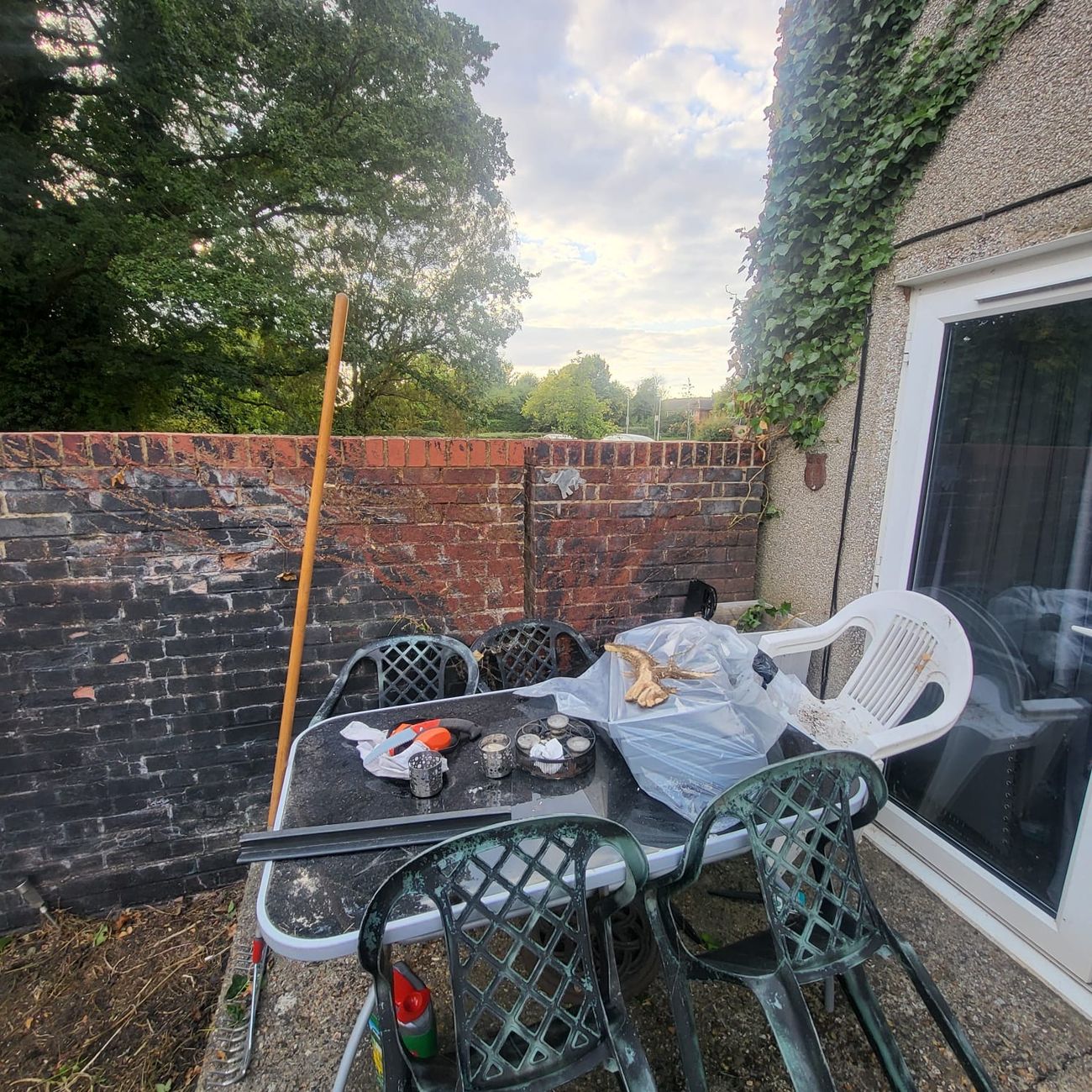 The patio and brick wall with the ivy off and the seating area clear — the corner of the garden the family actually sits in, handed back ready to use.